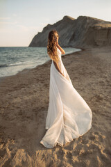Fototapeta na wymiar Attractive and happy bride in a fluttering luxury wedding gown with a big hem runs along the beach against mountains in the sunset light.