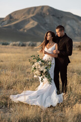 Fashionable portrait of a wedding couple in a picturesque field on the background of a mountain....