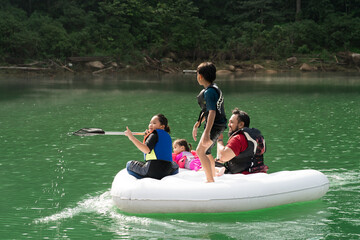 Family wearing life jackets paddling on an inflatable boat in Kenyir Lake, Malaysia.