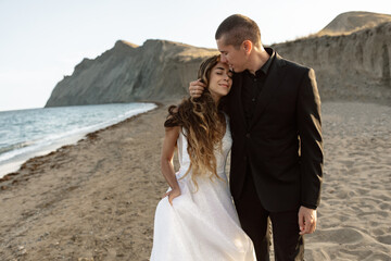 Sensual wedding couple hugging on the beach. The groom and bride against mountains and sea. The...