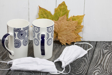 Two ceramic mugs. Before them are protective masks for the duration of the pandemic. Behind them...