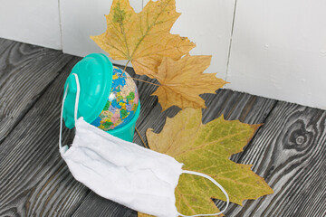 Garbage container with a globe. Nearby is a protective mask for a pandemic and dried maple leaves.