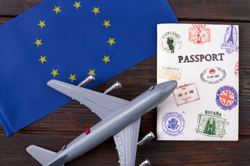 Flight to europe concept. European union flag with passport and toy airplane on dar wooden background.
