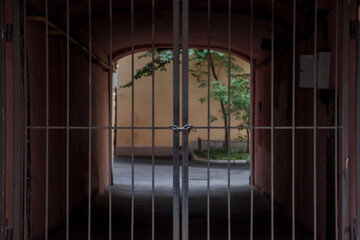 Beyond wrought-iron gates is an arch with light and greenery. Closed gates. Tied with metal chain and padlock. Light background outside gate. Concept of immigration with closed borders