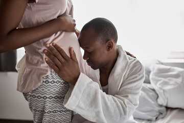 Obraz na płótnie Canvas young black husband cuddling pregnant wife on bed, touch her belly. happy relationships, pregnancy concept
