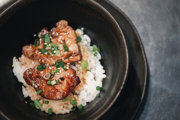 Grilled foie gras on top rice in black bowl.