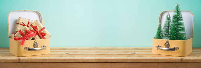 Winter holidays concept background with pine trees and gift boxes in suitcase on wooden table