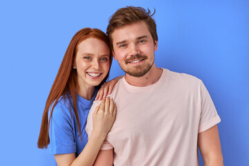 Obraz premium portrait of positive caucasian couple stand together isolated over blue background, posing at camera,wearing casual clothes, have perfect toothy smile