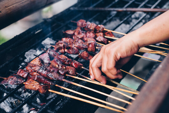 Hand grilling pork liver in bamboo skewers over hot charcoal fire. Selective focus.