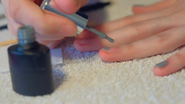 Woman is covering nails applying grey shellac gel polish at home, hands closeup. Girl making manicure at home for herself. Hygiene care about nails. Beauty procedure. Applying gray shellac on nail.