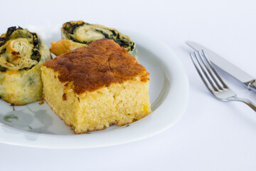 A slice of sweet cake and spinach pie in a plate on black surface with cutlery set.
