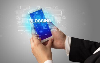 Female hand typing on smartphone with BLOGGING inscription, social media concept