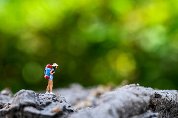 Miniature adventure travel concept : Small woman toy figure backpacker is Hiking or travel through a forest. with background bokeh of green nature.