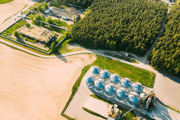 Aerial View Modern Granary, Grain-drying Complex, Commercial Grain Or Seed Silos In Sunny Spring Rural Landscape. Corn Dryer Silos, Inland Grain Terminal, Grain Elevators Standing In A Field