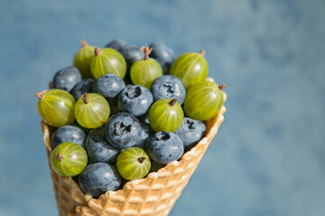 Blueberries and gooseberries in a waffle cone close up on a blue background.