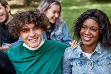 african and caucasian young people have rest together outdoors, smile and talk with each other, be friendly and tolerant