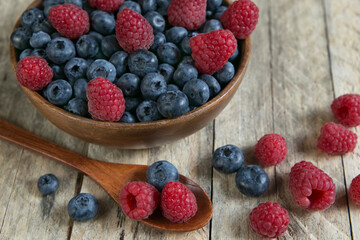 Blueberries and raspberries in a wooden bowl on an old wooden table with wooden spoon