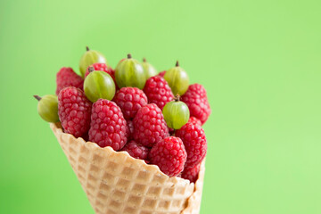 Raspberries and gooseberries in a waffle cone on a green background.