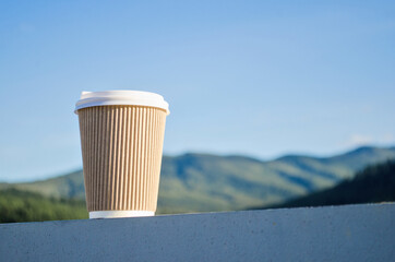 Brown disposable cup of coffee on the background of green carpathian mountains and blue sky