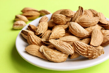 Almonds are not peeled on a white plate. Yellow background. View from above. Roasted almonds for a snack. Nuts. Food. Quenching hunger. Protein. Nuts in shells. Copy space