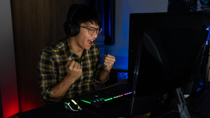 Fototapeta na wymiar Excited asian man pro gamer sitting at the table, playing and Winning in online video games on a computer and smartphone, technology gaming cyber or e-sport championship concept