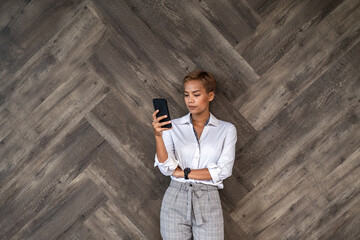 Serious business woman using mobile phone over brown wooden wall stock photo 