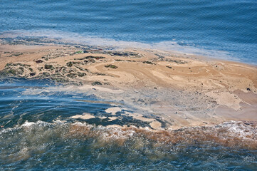 This horizontal image is an environmental shot of ocean water with pollution and an oil spill in the wake of a surf's wave.  This part needs attention to the eco-system of the sea.