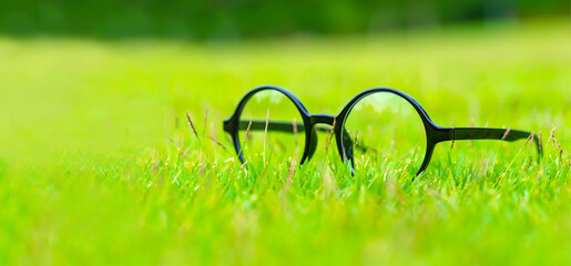 Looking for Natural Way Concept, Round shape eyeglasses lay on green grass in blurred landscape background