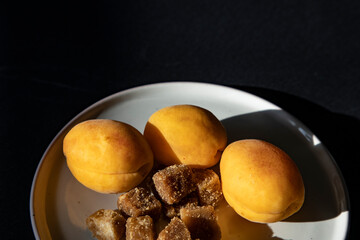 Apricots and brown sugar cubes on a white plate on a black background