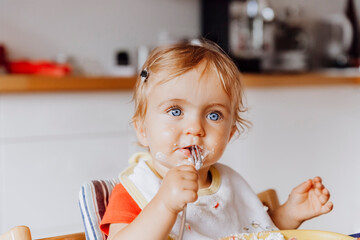 Toddler girl eating cake with a fork in kitchen