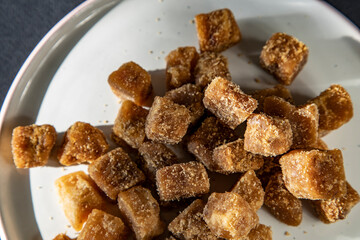 Brown sugar cubes on a white plate on a black background