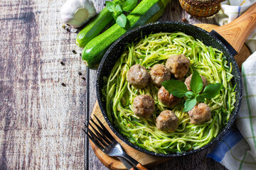 Healthy food. Cooked zucchini noodles with meatballs in a cast iron skillet on a rustic table. Copy space.