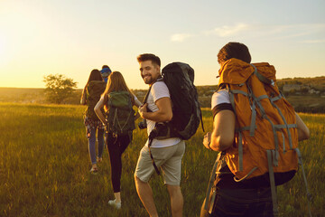 Hike. Hiking. Tourism.A group of tourists with backpacks are walking along the hill at sunset in nature in summer. - obrazy, fototapety, plakaty