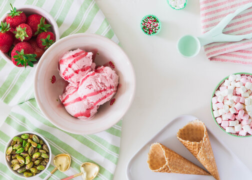 Summer dessert concept food photo with complementary colours of pink and green. Image depicts fresh fruit ice cream sweets nuts and candy with waffle cones in flat style.White background copy space