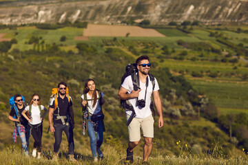 A group of friends with backpacks on a hike in nature. Young people tourists are walking on a hill...