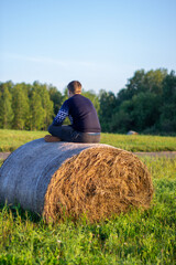 Naklejka na ściany i meble A Young boy sits on a hay bale and enjoys living happy on the country