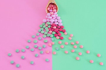 A close up unusual view point looking into an ice cream waffle cone which has sweets spilling out onto a bright colourful background of pink and green.  Candy treat food concept with copy space