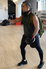 Motivated boot camp instructor stands with punch mitts in gym hall. Training with extended arm on...