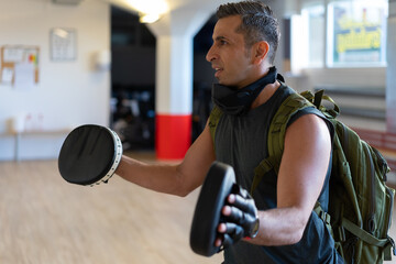 Motivated boot camp instructor stands with punch mitts in gym hall. Training with extended arm on wooden floor. Portrait for fitness concept.