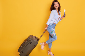 Full length shot of female in casual clothing walking with travel bag and documents, traveling abroad, has vacation in resort, waiting her plane, looks happy.