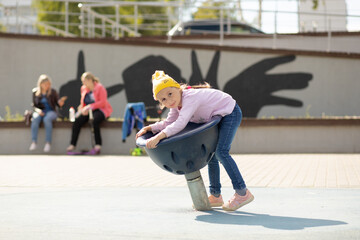 Little girl sits on a rotating bowl in the playground