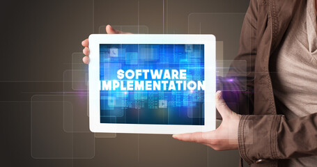 Young business person working on tablet and shows the inscription: SOFTWARE IMPLEMENTATION
