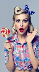 Excited woman with lollipop, dressed in Pinup style. Blond model in retro fashion and vintage concept studio shoot. Surprise or Shock emotion. Vertical banner composition. Studio image.