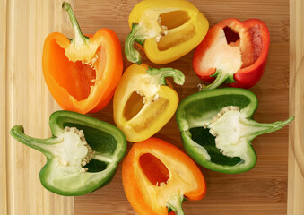 Colorful bell peppers on light beige wooden cutting board. Variety of multi colored capsicums. Top view. Bell pepper sliced into halves.