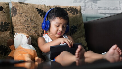 Cute Asian boy with headphones enjoys music on tablet, Keep your hands on the headphones concept.