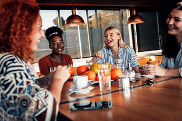 Group of young female friends having fun in cafe, talking and laughing while sitting at table.