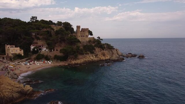 vuelo de dron sobre el mar mediterraneo espa&ntilde;ol, en la costa brava, llegando a un castillo al borde del mar, con agua cristalina verde turquesa 