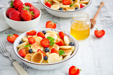 Pancake cereal, mini pancakes in a bowl with fresh strawberries, blueberries and honey. Trend food. Horizontal, copy space.