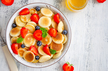 Pancake cereal, mini pancakes in a bowl with fresh strawberries, blueberries and honey. Trend food. Horizontal, top view, copy space.