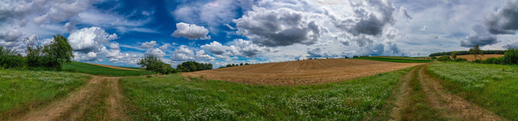 An ultra wide angle image of a green field, two roads on the sides and a blue sky with beautiful white clouds